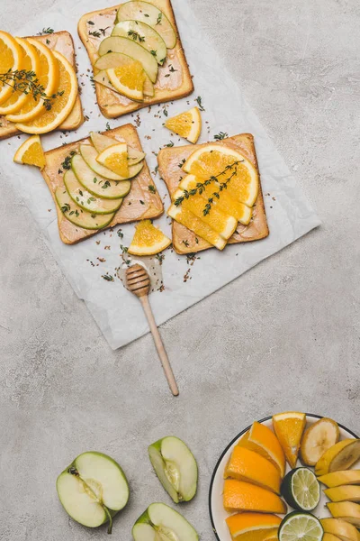 Vista superior de sándwiches saludables con frutas frescas y cazo de miel en gris - foto de stock