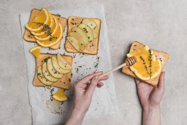 Recortado tiro de persona verter miel en delicioso sándwich con rodajas de naranja - foto de stock