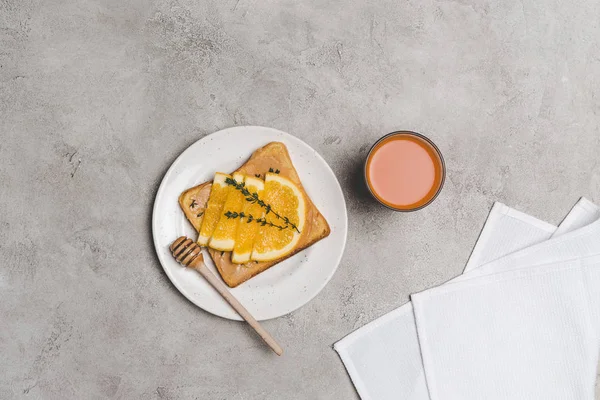 Vista superior de sándwich saludable con rodajas de miel y naranja y vaso de jugo fresco en gris - foto de stock