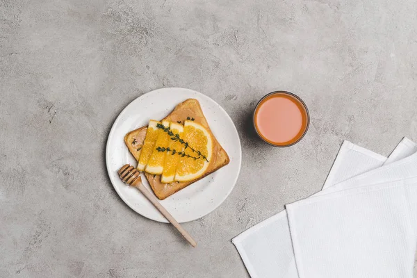 Blick von oben auf gesundes Sandwich mit Honig und Orangenscheiben und einem Glas frischen Saft auf grau — Stockfoto