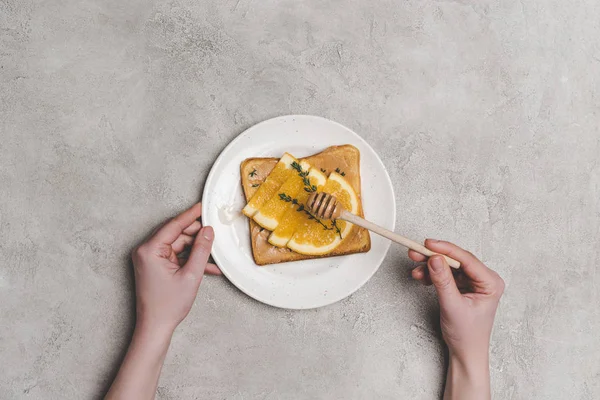 Vista superior de las manos humanas con cazo de miel y sándwich saludable con rodajas de naranja en gris - foto de stock