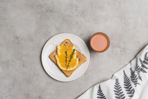Sándwich con miel y rodajas de naranja y vaso de jugo fresco sobre gris - foto de stock