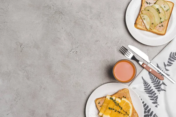 Vista superior de sándwiches saludables con miel y rebanadas de frutas y vaso de jugo fresco en gris - foto de stock