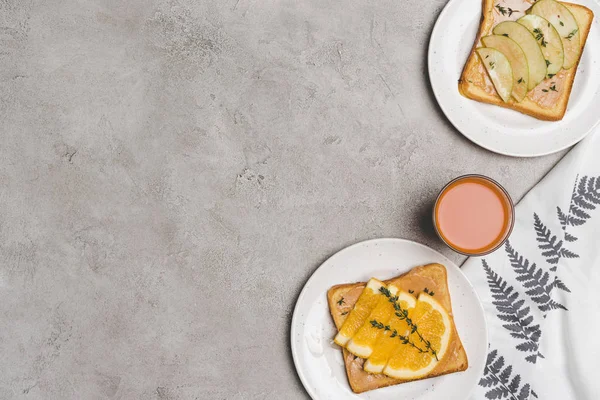 Vista superior de tostadas saludables con miel y rebanadas de frutas y vaso de jugo fresco en gris - foto de stock