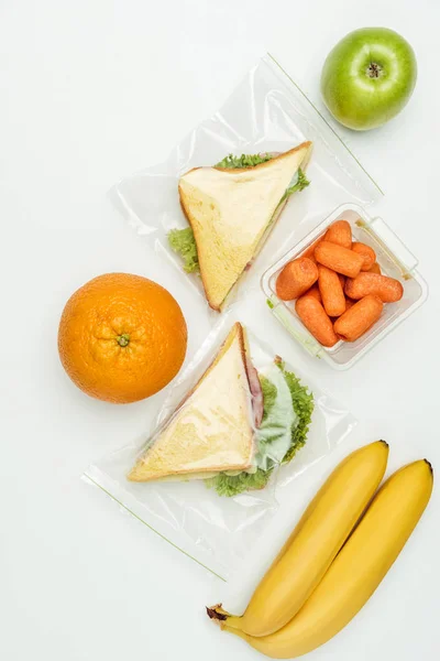 Blick von oben auf Früchte und Sandwiches in Reißverschlusstaschen isoliert auf weiß — Stockfoto