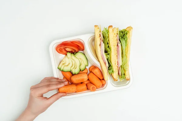 Immagine ritagliata di donna che prende la carota dalla scatola del pranzo isolata su bianco — Foto stock