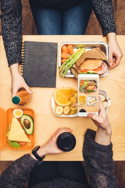 Imagen recortada de la mujer sentada en la mesa y tomando una foto del almuerzo con el teléfono inteligente - foto de stock