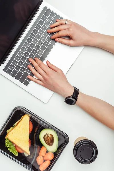 Cropped image of woman using laptop at table with food in lunch box isolated on white — Stock Photo