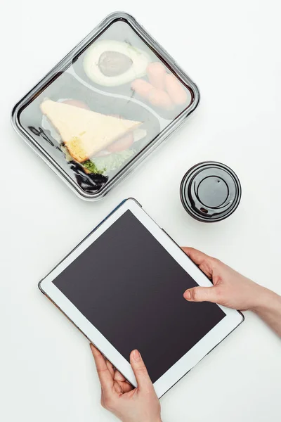 Cropped image of woman holding tablet at table with food in lunch box isolated on white — Stock Photo