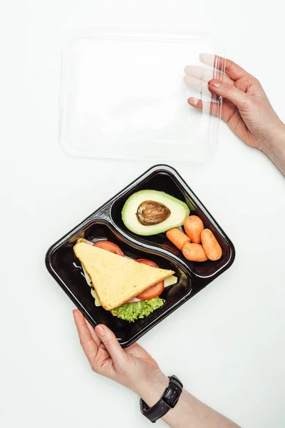 Imagem cortada de mulher abrindo caixa de almoço de plástico com alimentos isolados em branco — Fotografia de Stock