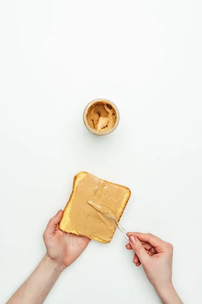 Imagen recortada de la mujer poniendo mantequilla de maní en el pan aislado en blanco - foto de stock