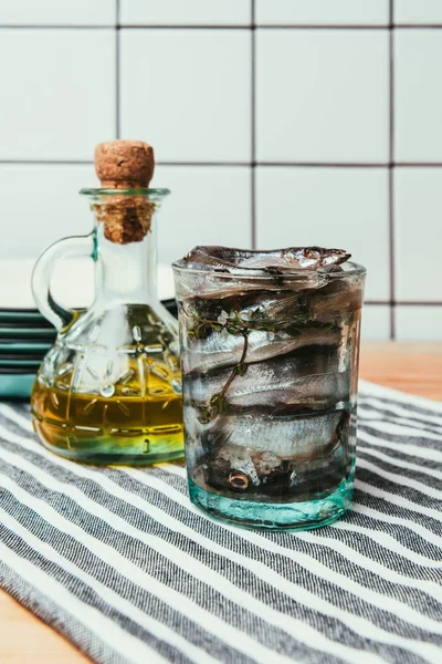 Front view of pile of salted fish in glass on towel with bottle of oil and plates behind — Stock Photo