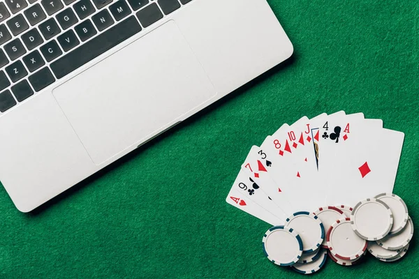 Playing cards and chips on casino table by laptop — Stock Photo