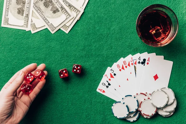 Женская рука держит кости за столом казино с деньгами и картами — стоковое фото