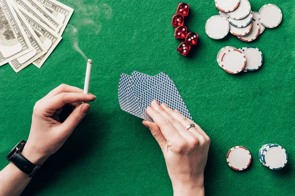 Mujer sosteniendo cigarrillo y jugando a las cartas por mesa de casino - foto de stock