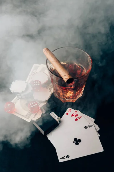 Vaso con whisky y cigarro en la mesa con tarjetas y dinero - foto de stock