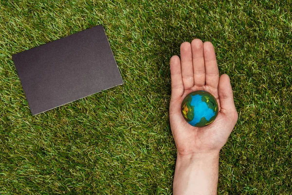 Imagen recortada del hombre sosteniendo el modelo de tierra en la mano, pizarra sobre hierba verde, concepto de día de la tierra - foto de stock