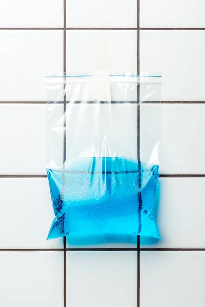 Bolsa de plástico ziplock con agua azul colgando en la pared del azulejo, concepto de día de tierra - foto de stock
