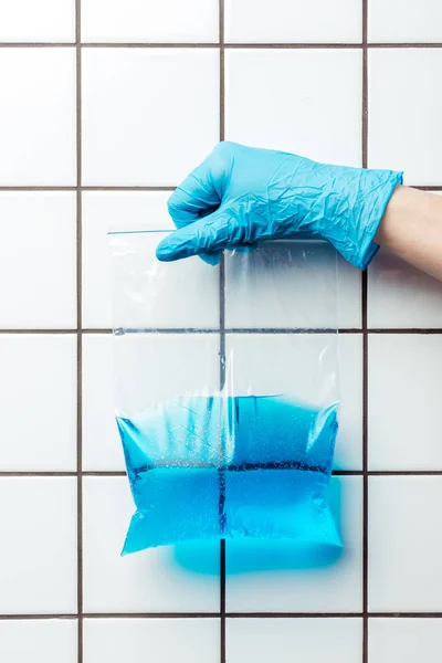 Immagine ritagliata della donna in guanto di gomma blu tenuta sacchetto di plastica con zip con acqua blu, concetto giorno terra — Foto stock