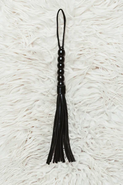 Black strict leather flogging whip on white carpet — Stock Photo