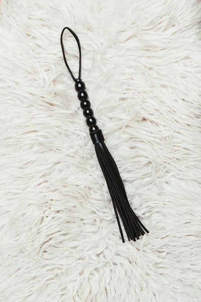 Black leather flogging whip on white carpet — Stock Photo