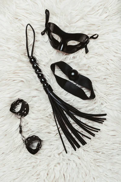 Black bdsm gag with whip and mask on white carpet — Stock Photo