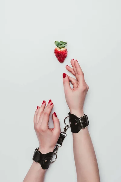 Mãos femininas amarradas com algemas de couro chegando para morango isolado em branco — Fotografia de Stock