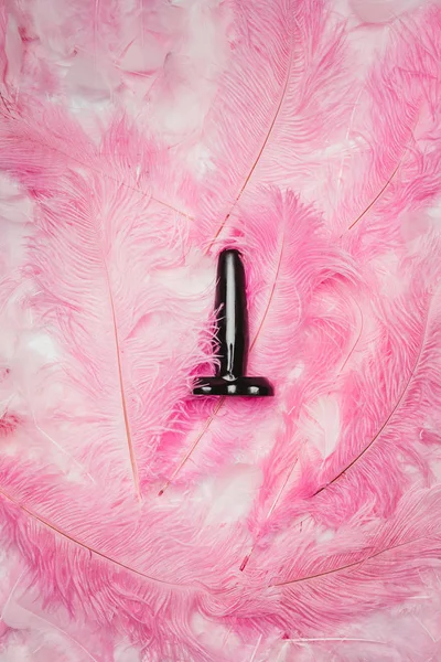 Black butt plug toy on pink feathers — Stock Photo