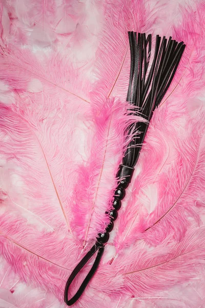 Black strict leather flogging whip on pink feathers — Stock Photo