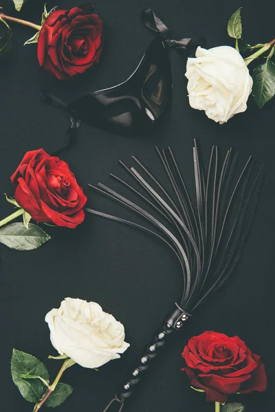 Fouet et masque en cuir noir avec des fleurs roses isolées sur noir — Photo de stock