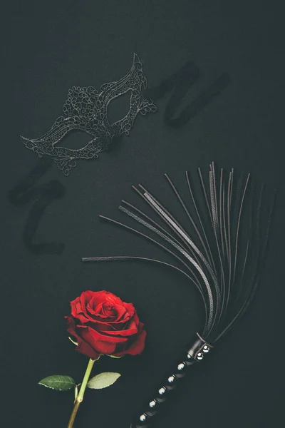 Lacy mask and black whip with rose flower isolated on black — Stock Photo