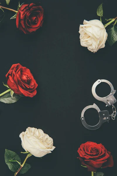 Metall-Handschellen mit Rosenblüten isoliert auf schwarz — Stockfoto