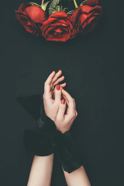 Female hands tied with ribbon and rose flowers isolated on black — Stock Photo