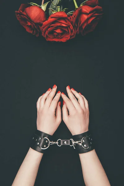 Black leather cuffs on female hands and rose flowers isolated on black — Stock Photo