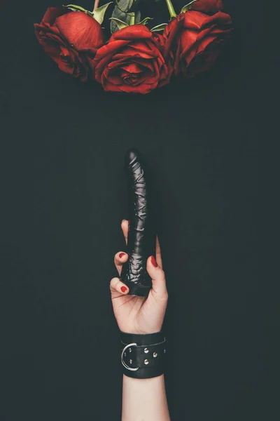 Black dildo in female hand by red roses isolated on black — Stock Photo