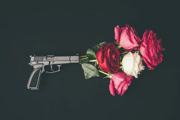 Gun shooting with bouquet of rose flowers isolated on black — Stock Photo