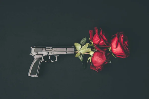 Red roses in gun barrel isolated on black — Stock Photo