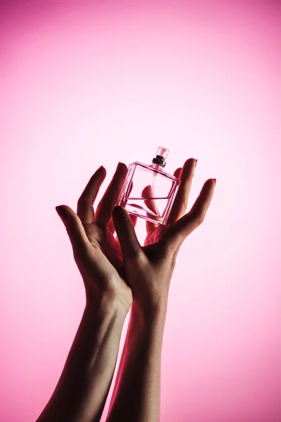 Vista ritagliata della donna in possesso di bottiglia di profumo, isolato su rosa — Foto stock