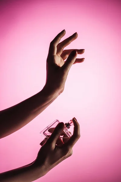 Vista recortada de la mujer sensual rociando perfume en la mano, aislado en rosa - foto de stock