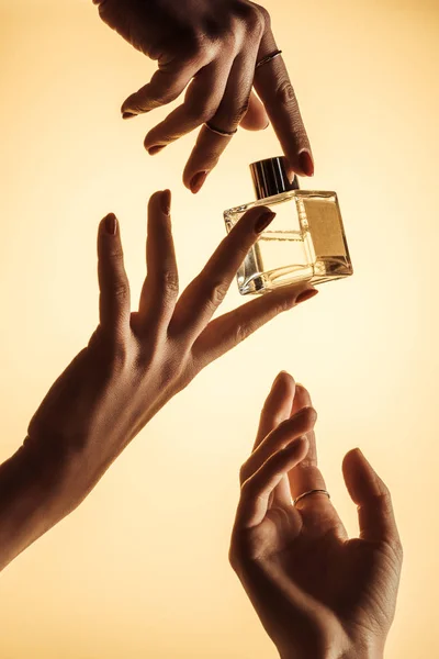 Cropped view of female hands with perfume, isolated on yellow — Stock Photo
