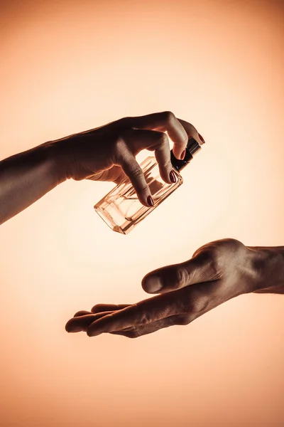 Обрізаний вид жінки, що розбризкує парфуми на чоловічій руці, ізольований на помаранчевому — стокове фото