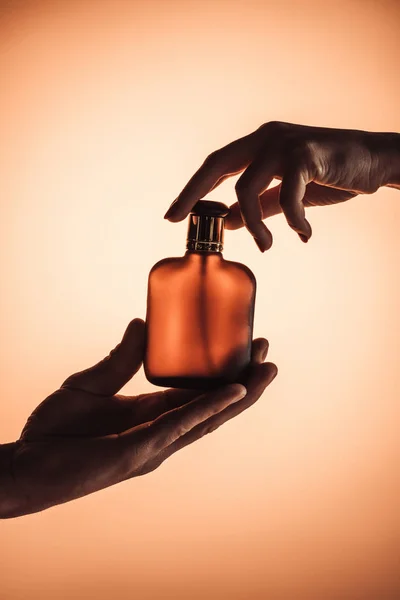 Cropped view of man and woman holding one bottle of perfume, isolated on orange — Stock Photo