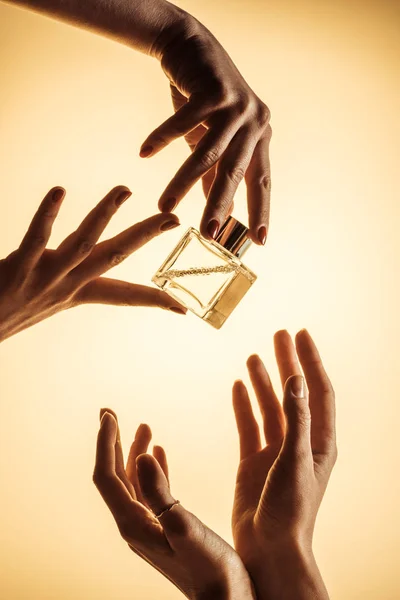 Обрізаний вид жінок, що тримають розкішну пляшку парфумів, ізольовані на жовтому — стокове фото
