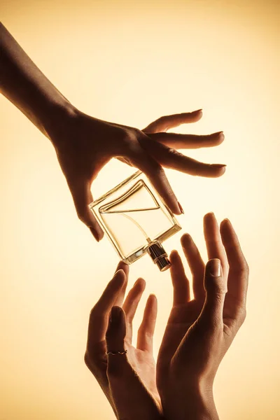 Cropped view of women holding luxury perfume bottle, isolated on yellow — Stock Photo