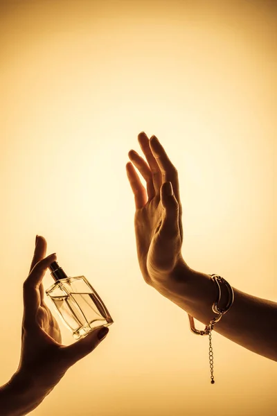 Abgeschnittene Ansicht einer Frau, die Parfüm auf die Hand sprüht, um Duft zu fühlen, isoliert auf gelb — Stockfoto