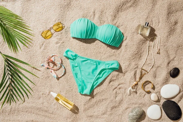 Blick von oben auf stilvollen blauen Bikini mit verschiedenen Accessoires und Kieselsteinen am Sandstrand — Stockfoto