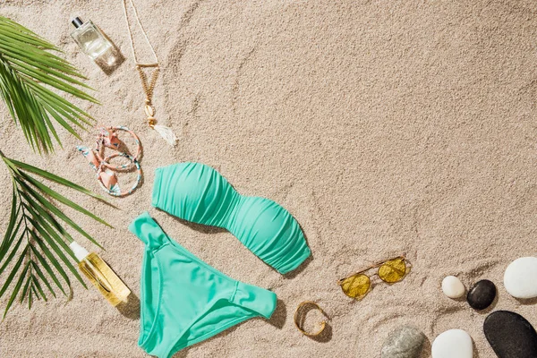 Vista superior de bikini azul con varios accesorios y guijarros en la playa de arena — Stock Photo