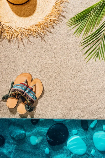 Vue de dessus des tongs élégantes et chapeau de paille sur la plage de sable — Photo de stock