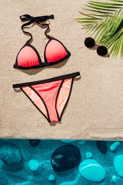 Vista superior del elegante bikini rosa con gafas de sol en la playa de arena - foto de stock