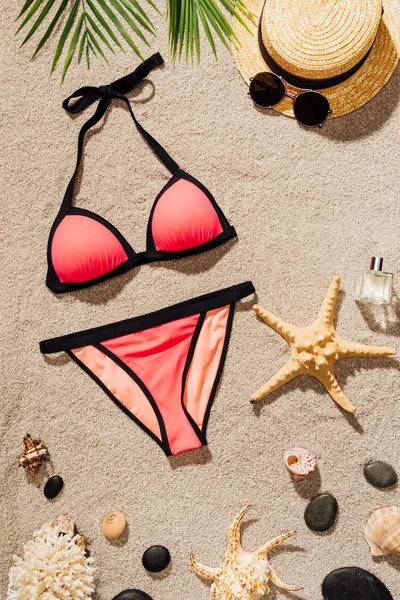 Vista superior de bikini rosa con accesorios y perfume en la playa de arena - foto de stock